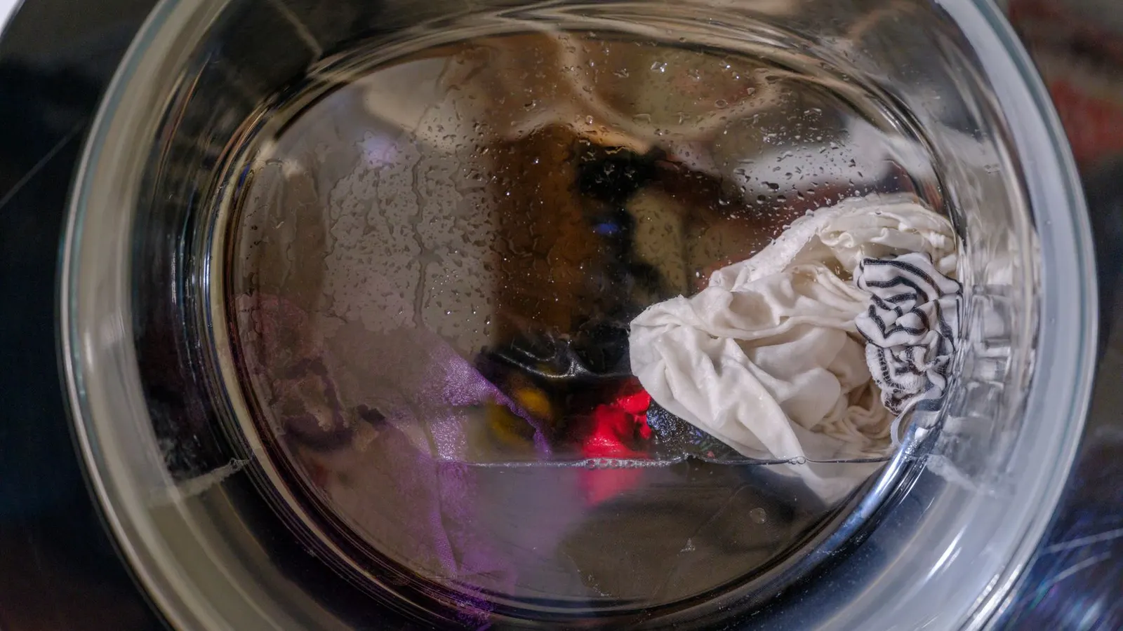 A clear view of wet clothes spinning inside a front-loading washing machine.