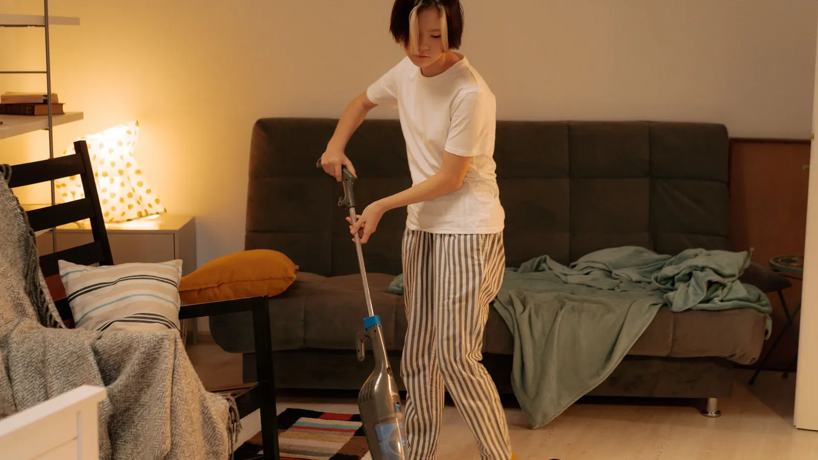 Asian woman cleaning a messy living room at home with a vacuum cleaner, creating a tidy space.