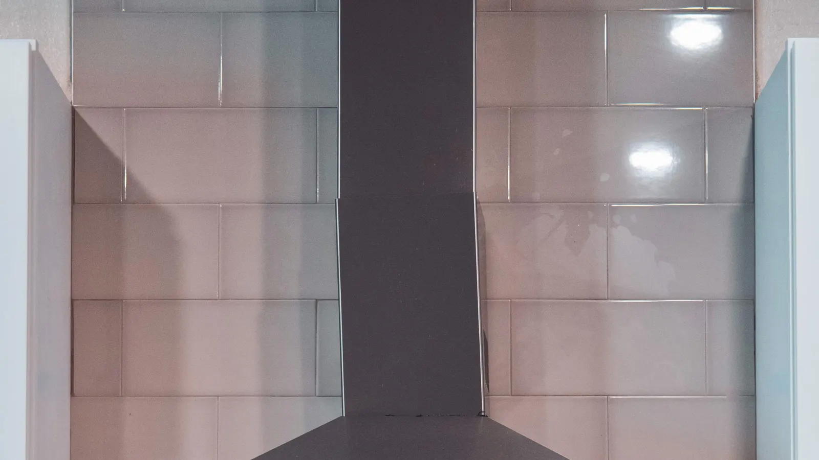 Dark wall-mounted range hood above a glossy tiled backsplash.