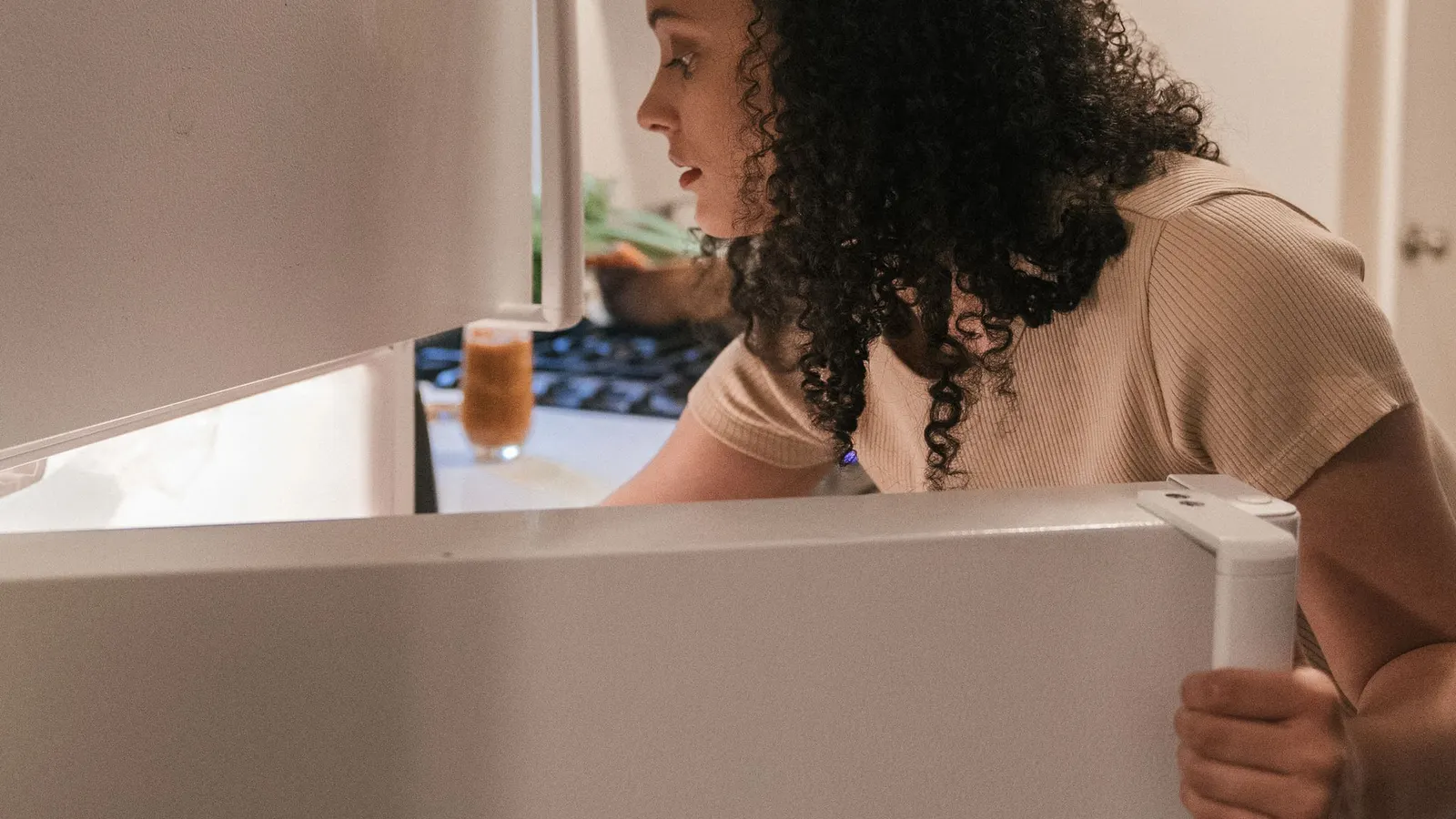 Woman looking inside an open household refrigerator.