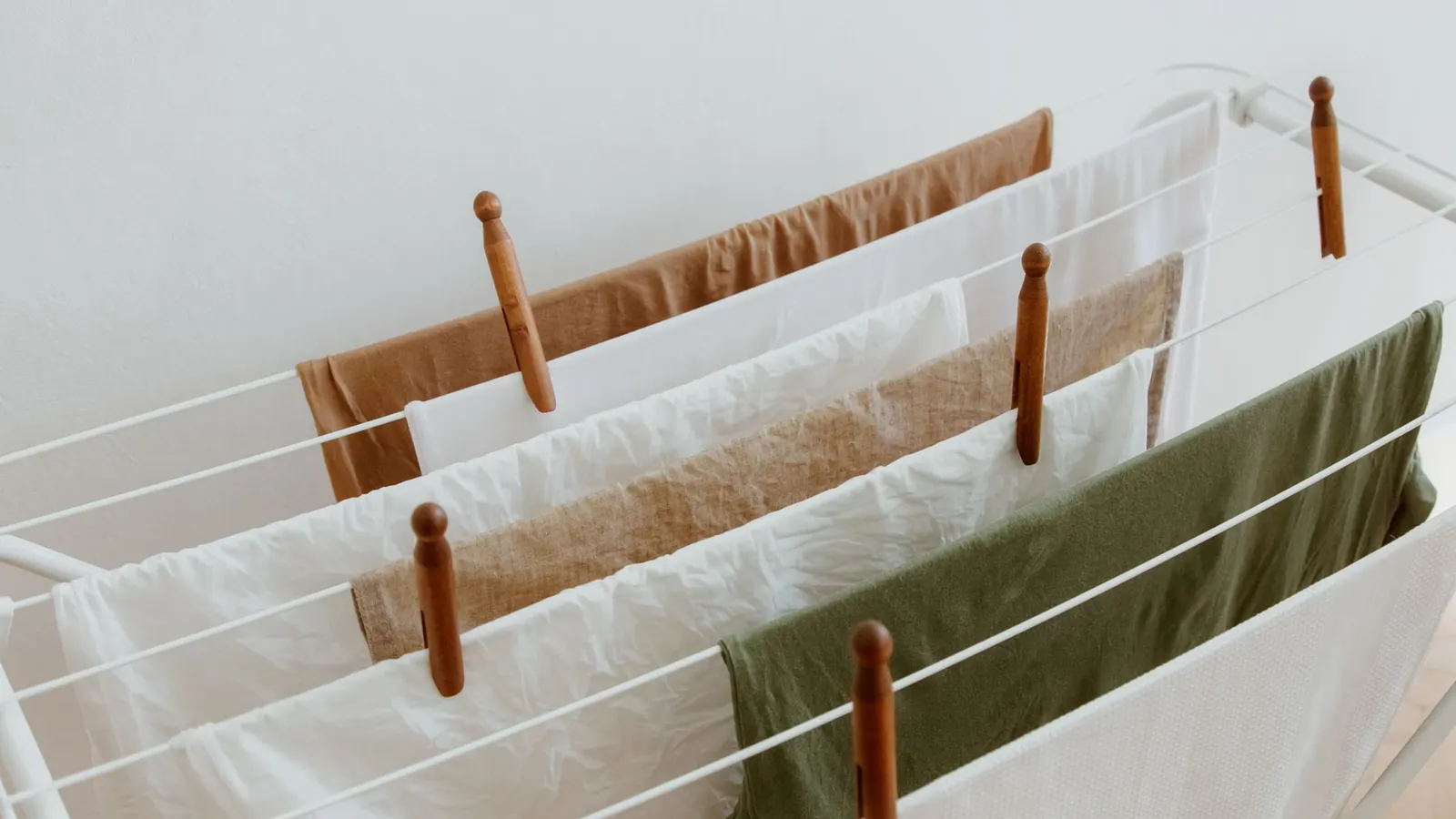 Light-colored laundry hanging from an indoor drying rack with wooden pegs.
