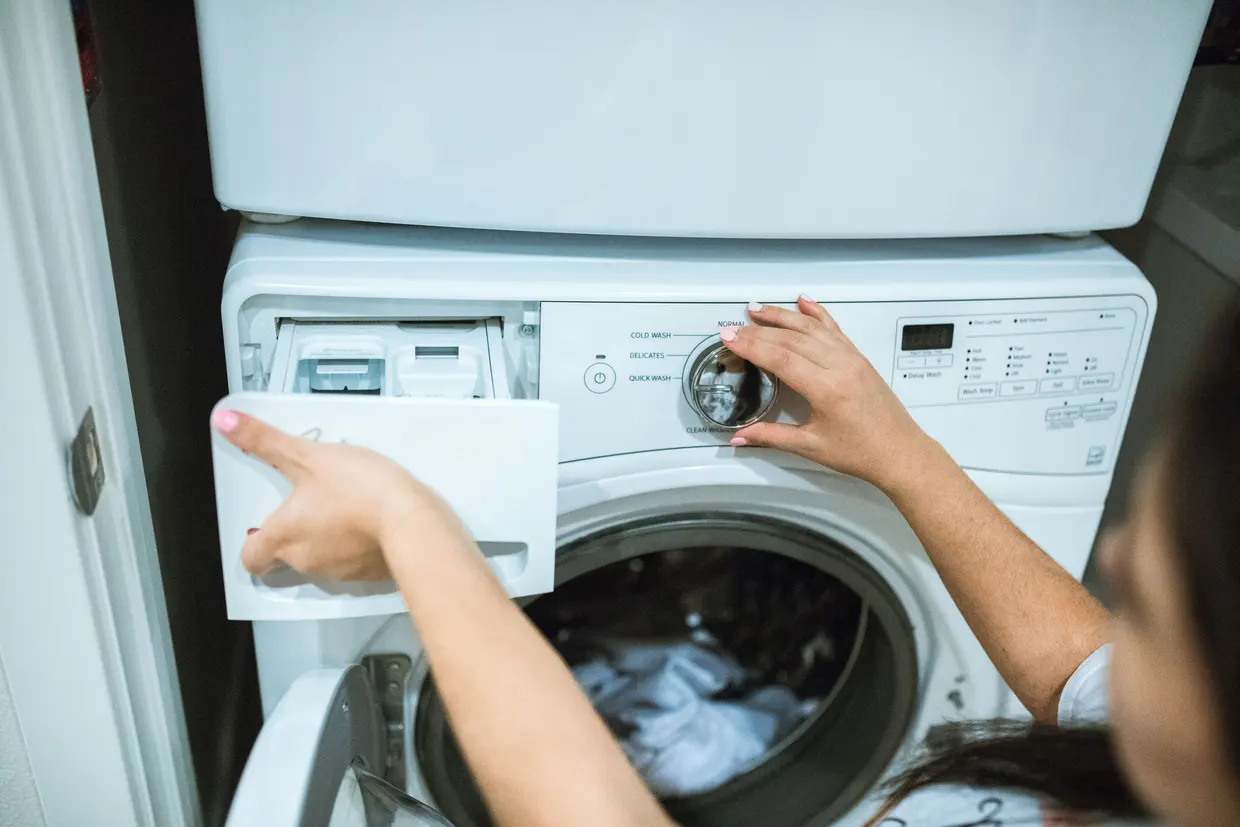 A person adjusting a washing machine with the detergent drawer open