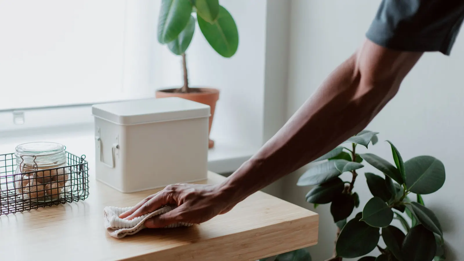 Hand wiping a sealed wooden tabletop with a soft cloth.