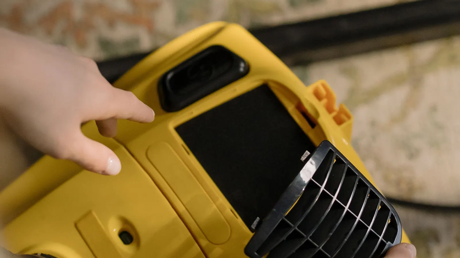 Hands removing a rectangular filter from a yellow upright vacuum cleaner.